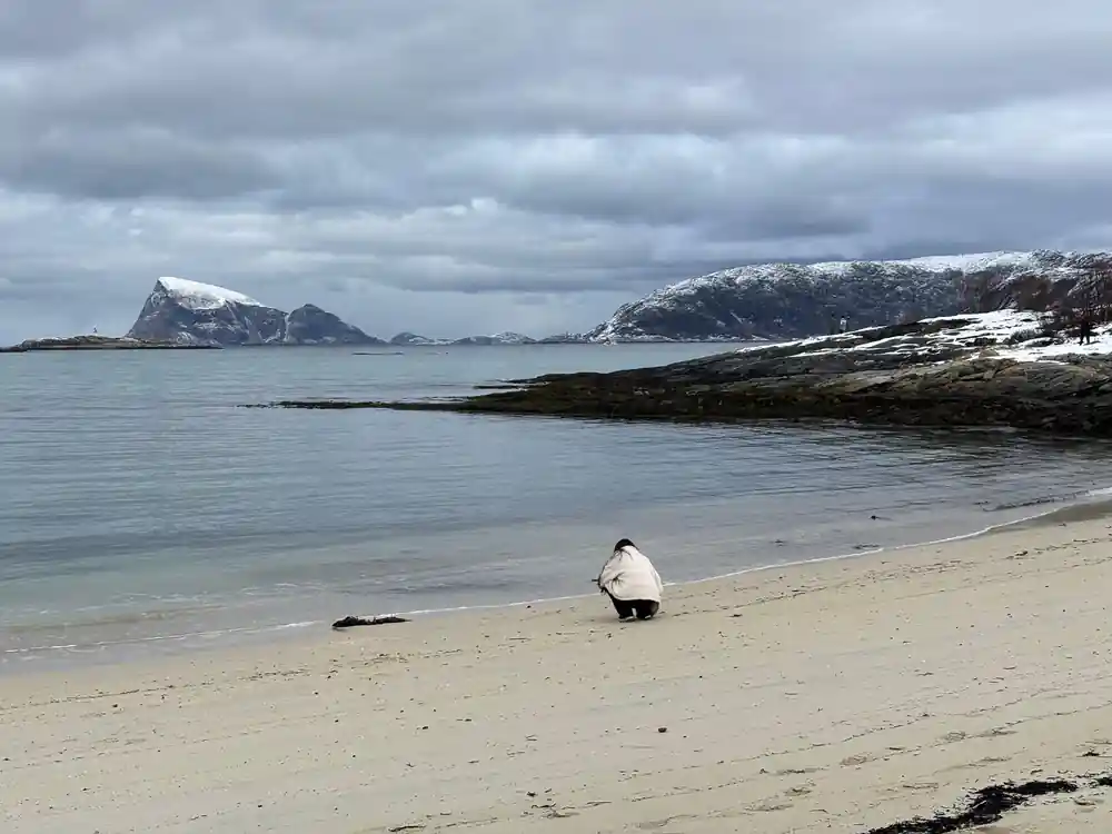 A guest crouching on a wide empty beach under cloud