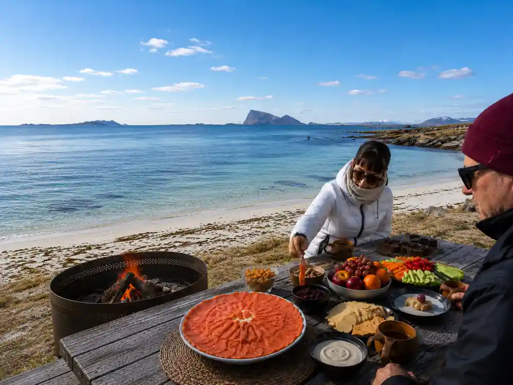 A guide laying out salmon and fruit on a table by the beach