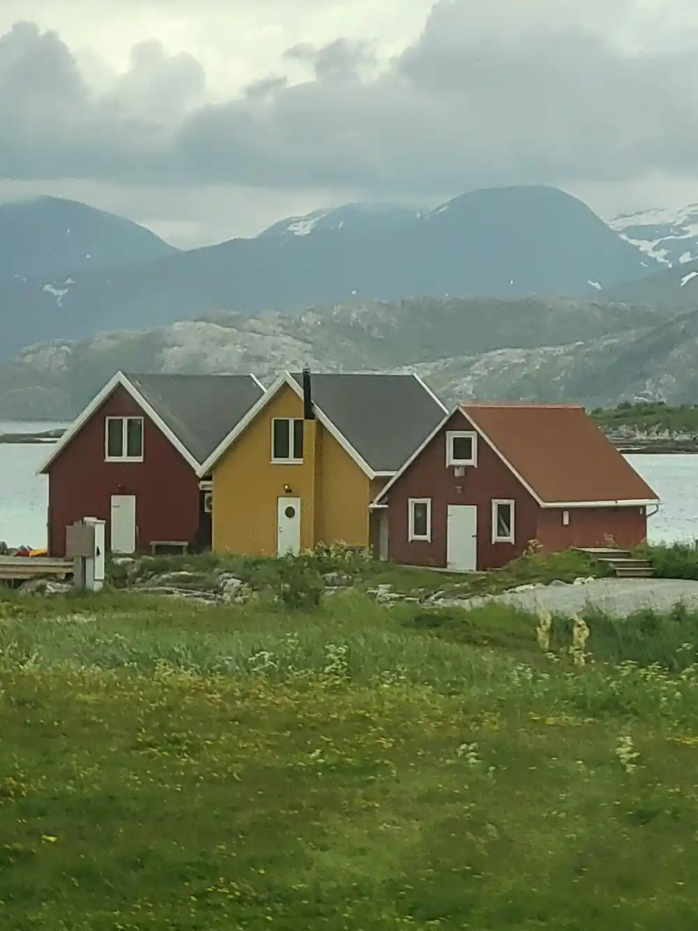 Red and yellow houses on grass beneath cloudy mountains